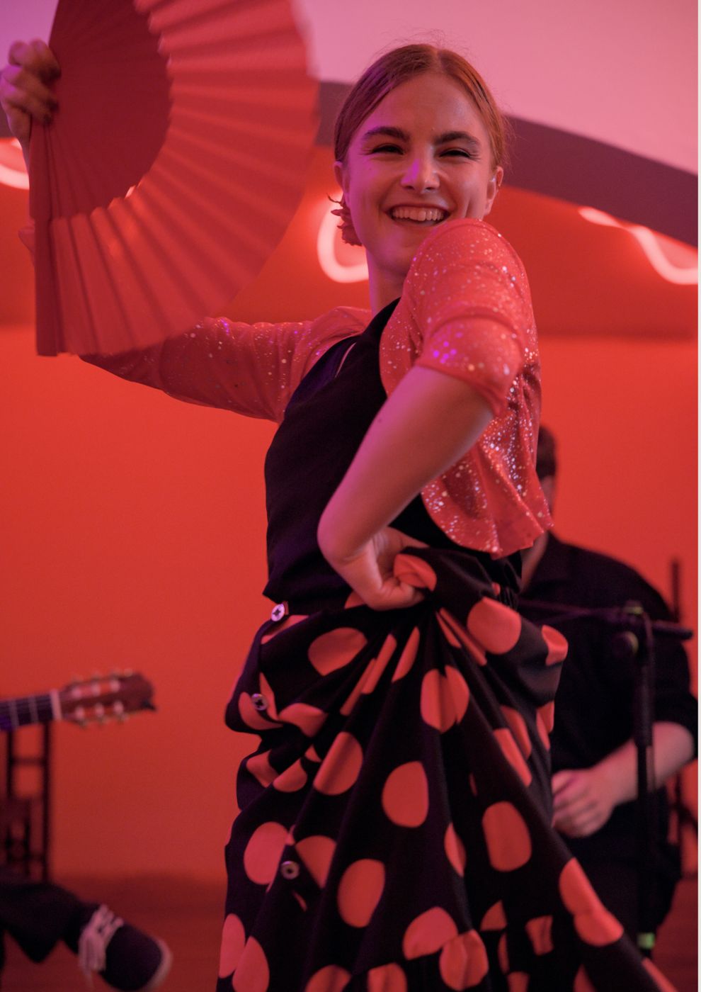 A smiling dancer with a fan and polka-dot skirt