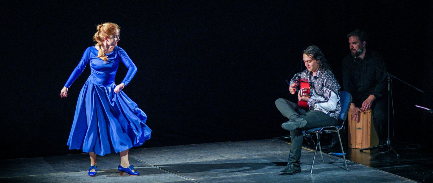 A dancer in blue with guitar and cajón on stage